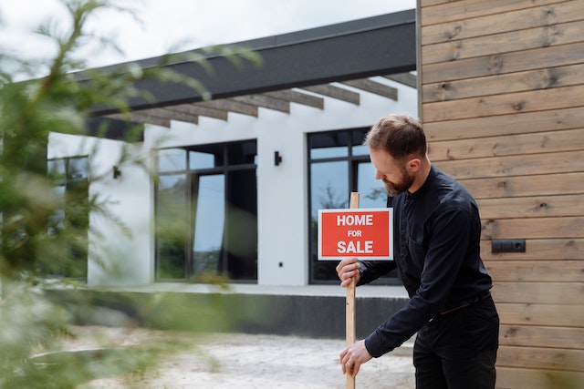 a person dressed in black setting up a home for sale sign